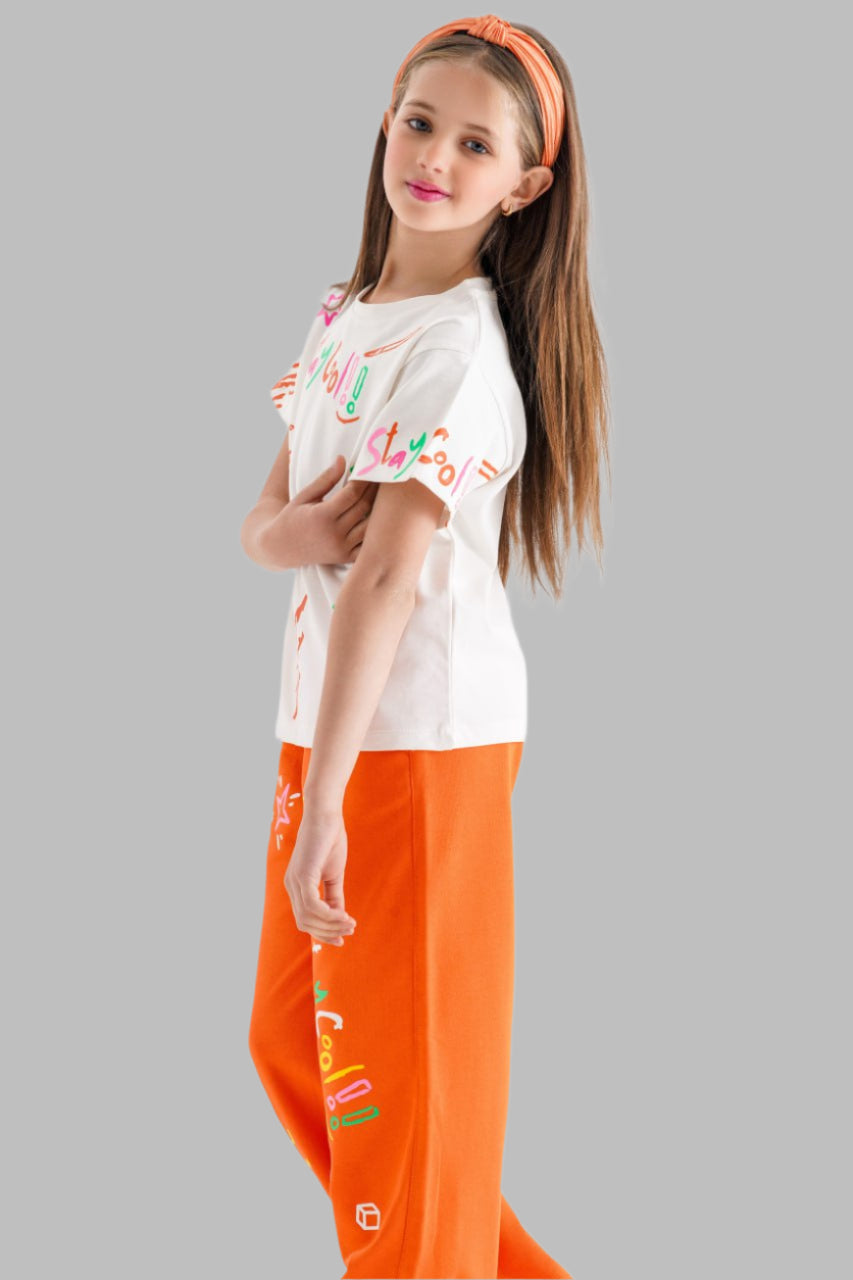 Young girl wearing a white shirt and orange pants with colorful designs on a white background